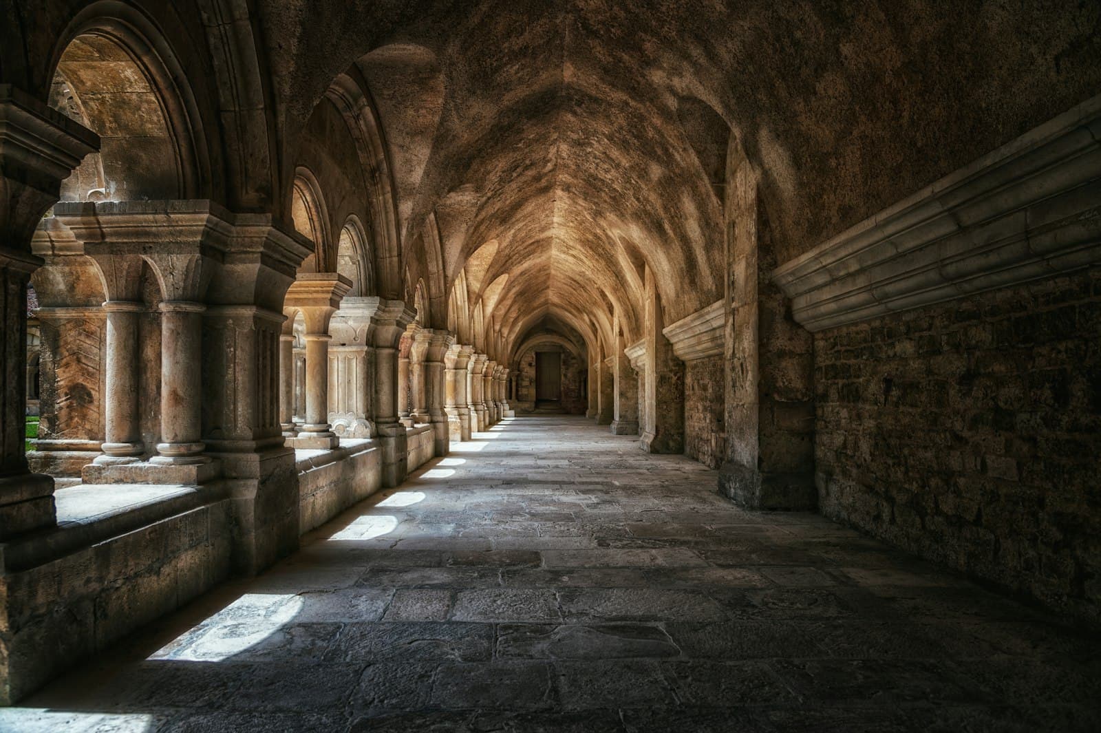 A long stone cloister receding into shadow — the den and ancient empires