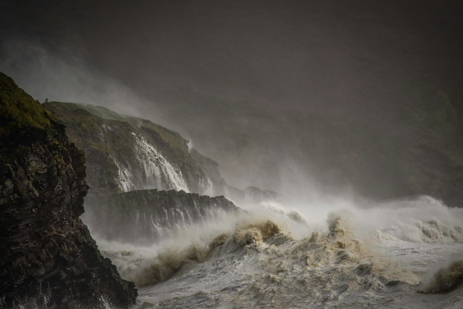 A storm-lashed coast under grey skies — suffering and unanswered questions